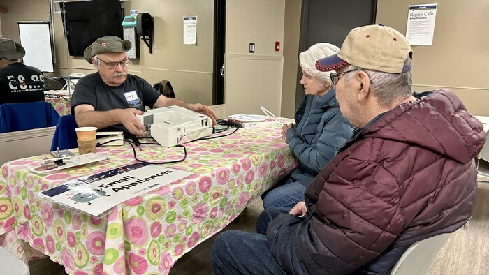 Un homme et une femme assis à une table en attendant que leur machine à coudre soit réparée lors du Repair Cafe à Okotoks en mars 2023.