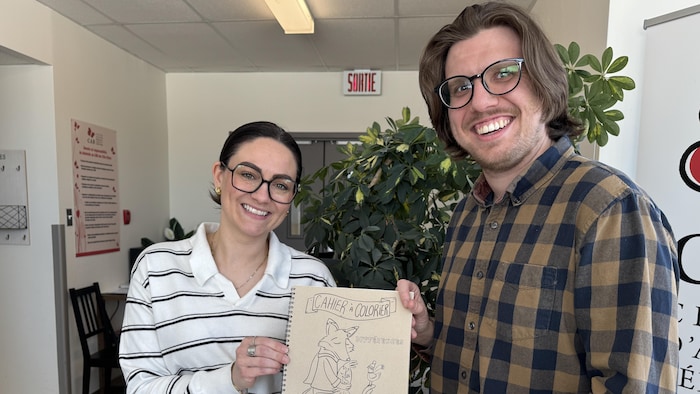 Philippe Beauchemin et Amélie Therrien tiennent un cahier è colorier entre leurs mains et sourient à la caméra.