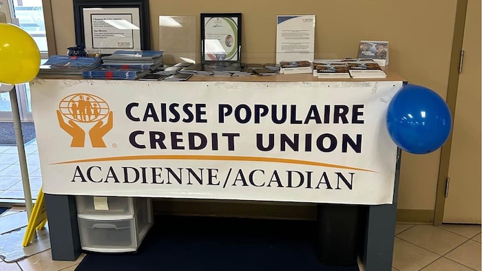 Une bannière de la caisse populaire devant une table décorée de ballons à l'hélium, à l'intérieur de la succursale.