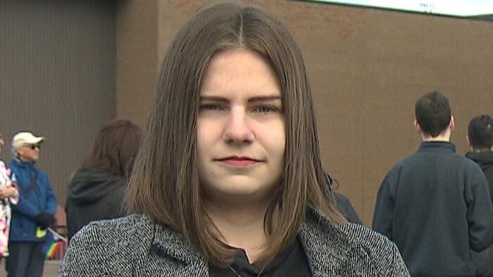 Une jeune femme lors d’une mobilisation devant une école regarde la caméra d’un air sévère. 