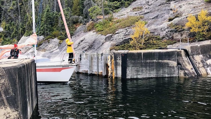 Une photo prise depuis le quai, montrant un voilier qui s'engage dans l'étroit passage de l'écluse de la cale sèche.