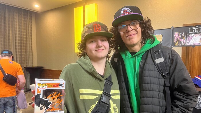 Deux jeunes participants posent pour une photo, l'un d'eux tenant une boîte de figurine de collection Funko Pop! du personnage Goku, de la série Dragon Ball Z.