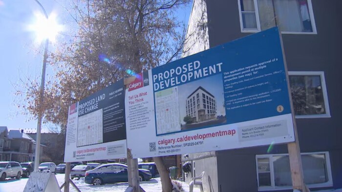 Un grand panneau d'affichage de la Ville de Calgary annonce une proposition de développement immobilier et de changement d'affectation du sol devant un bâtiment résidentiel.