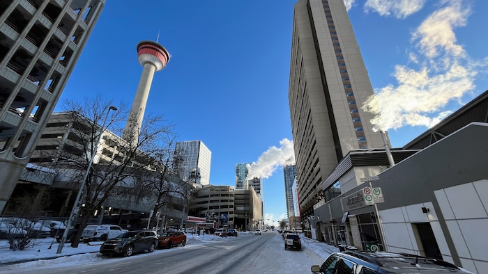 Une rue enneigée du centre-ville de Calgary, bordée de gratte-ciel et de garages de stationnement, s'étend sous un ciel bleu dégagé.