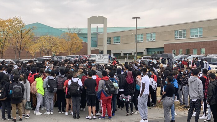 Un groupe de jeunes, la plupart de dos, rassemblés devant une école.