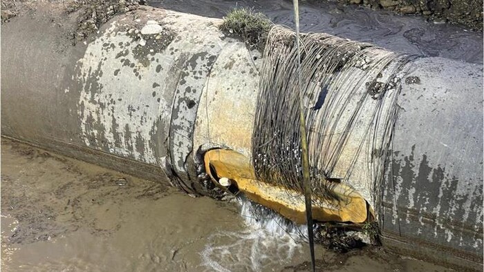 Une vue rapprochée montre un bris majeur sur une conduite d'eau de grand diamètre située dans une fosse d'excavation.