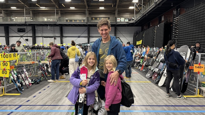 Jamie Kotlewski serre chaleureusement ses deux petites filles contre lui, des sourires radieux aux lèvres et leurs tout premiers skis à la main.
