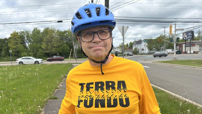 Un homme en vélo, portant un casque, sourit à la caméra.