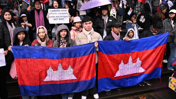 Des manifestants tiennent des drapeaux cabodgiens, des Pancartes et des parapluies.