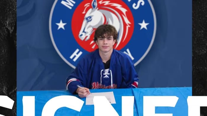 Cameron Casorso assis à une table devant une affiche du Club des Mustangs regarde l'objectif en signant un document.