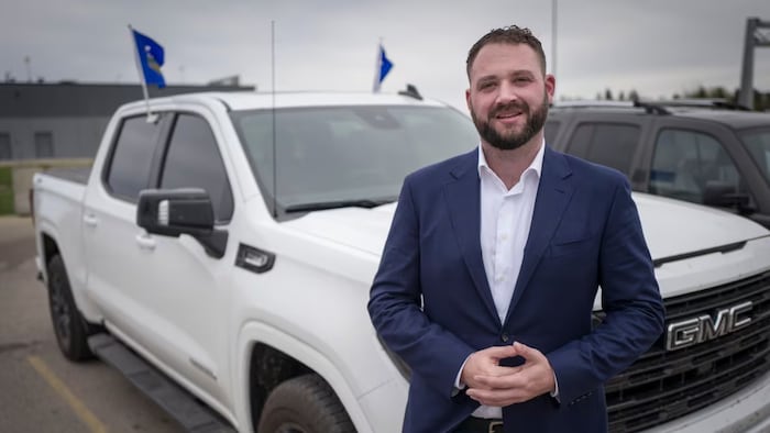 Un homme se tient devant un véhicule blanc et fixe l'objectif d'une caméra, en Alberta.