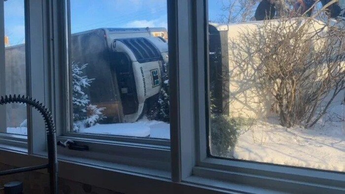 Photo d'un camion semi remorque étalé dans la neige à quelques mètres d'une maison.