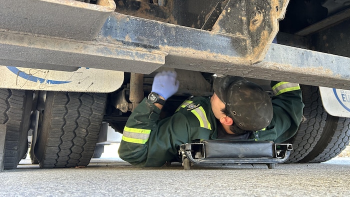 Un individu, installé sur une plaque roulante, effectue une inspection du dessous d'un camion.