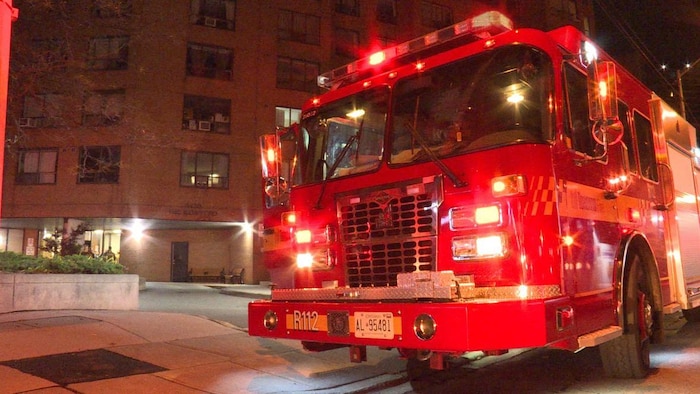 Un camion de pompier rouge aux lumières clignotantes devant un immeuble en briques brunes, le soir.