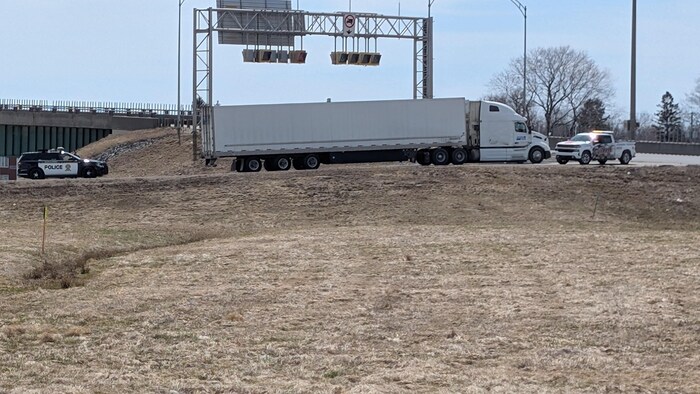 Un camion se trouve bloqué par des véhicules d'urgence dans une bretelle d'accès d'autoroute. 