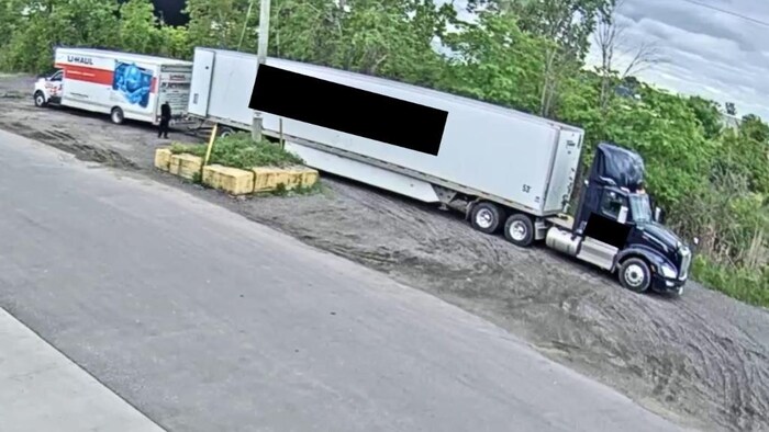 Une capture d'écran montre une fourgonnette U-Haul derrière un gros camion. Un individu est debout entre les deux.