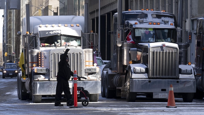 Un passant près de deux camions lourds stationnés dans une rue à Ottawa.