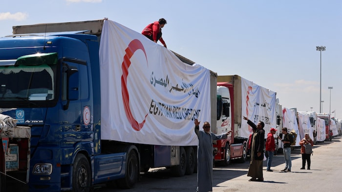 Une file de camions identifiés par de grandes banderoles du Croissant-Rouge égyptien.