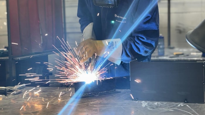 Un soudeur soude une pièce de métal. Des étincelles et un arc de lumières se dégagent s de la pièce.