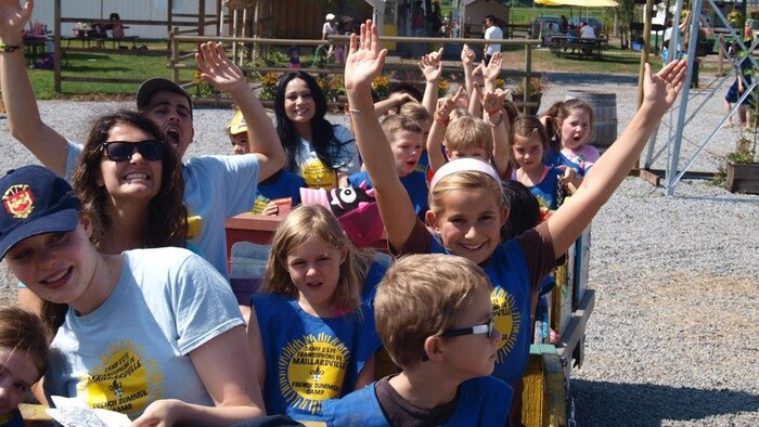 Les enfants et les animateurs sont assis dans un wagon et lèvent les bras au ciel en souriant.