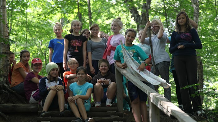 Des jeunes sont assis dans un escalier de bois en plein air, d'autres sont debout derrière eux et tous sourient à la caméra.