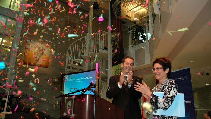 Un homme et une femme applaudissent tandis que des confettis tombent du haut d'une salle.