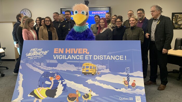 Plusieurs personnes debout, en arrière d'une grand pancarte pour sensibiliser à la sécurité routière des enfants.