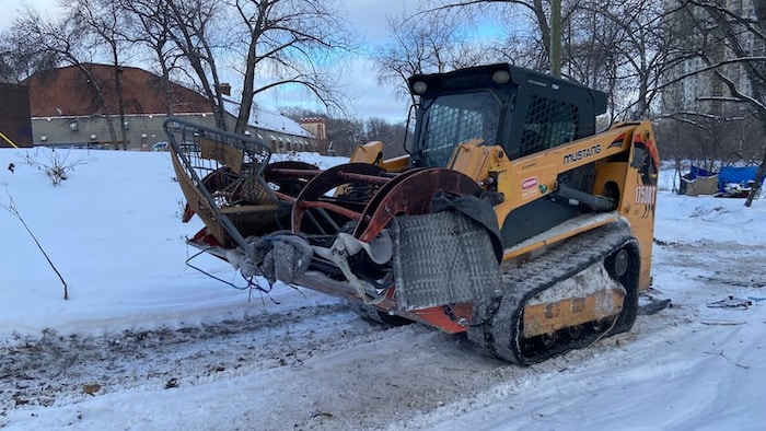 Une petite tractopelle transporte des débris de meubles et des couvertures à l'extérieur dans la neige.