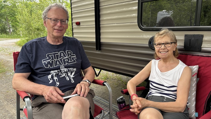 Deux campeurs assis sur des chaises de camping devant leur roulotte.
