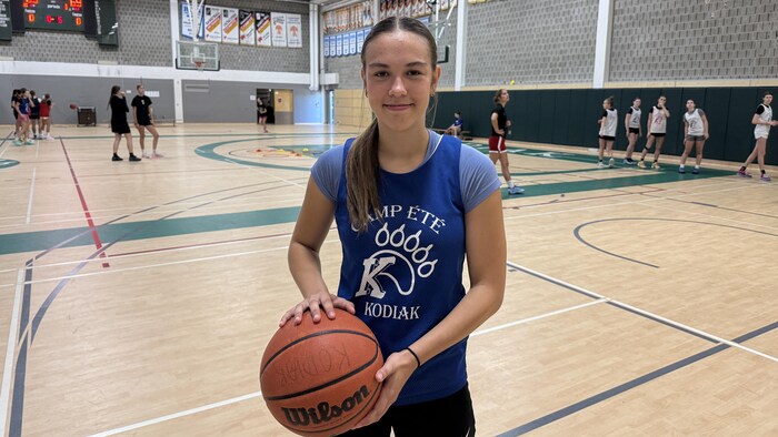 Olivia Frenette pose avec un ballon dans les mains sur un court de basketball.