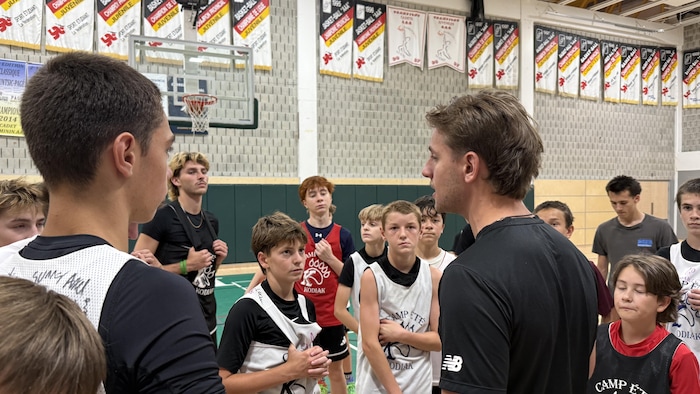 Antoine St-Jean donne des instructions à des joueurs de basketball dans un gymnase.