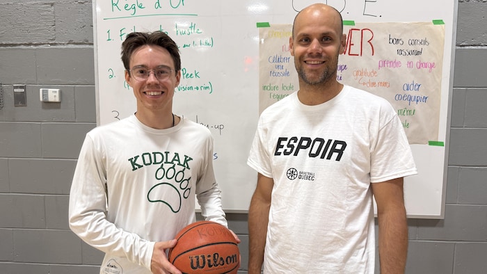 Émile Asselin, un ballon dans les mains, et Christian Deshaies, posent devant un tableau.