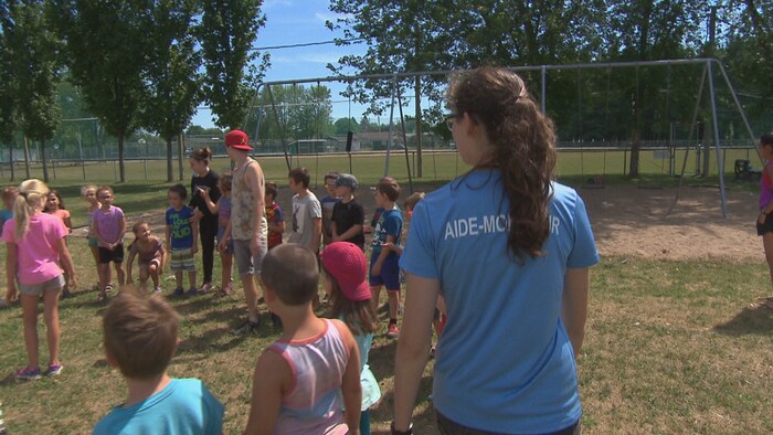 Une monitrice tourne autour d'un groupe d'enfants dans un parc. 