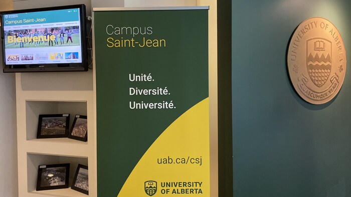 Une bannière et une plaque sur un mur du Campus Saint-Jean avec un message de bienvenue sur une télévision.