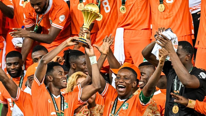 Les joueurs de l'équipe nationale de Côte d'Ivoire, vêtus de leur maillot orange, brandissent la coupe de la compétition de la Coupe d'Afrique des Nations.