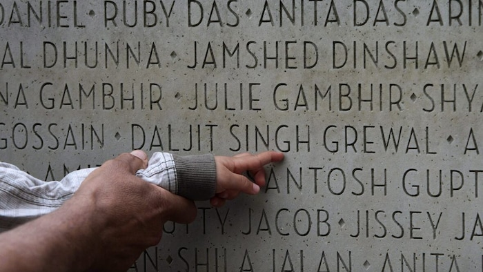 Le doigt d'un bébé qui pointe un mur sur lequel des noms sont gravés.