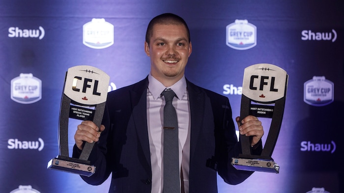 Un joueur de football en complet pose avec ses deux trophées.