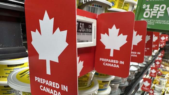 Des affiches rouges, ornées de feuilles d'érable, sur des étagères à l'épicerie.