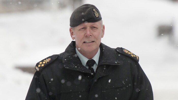 Un homme marche sous la neige, il est vêtu d'un manteau à épaulettes de l'armée et d'un béret assorti.