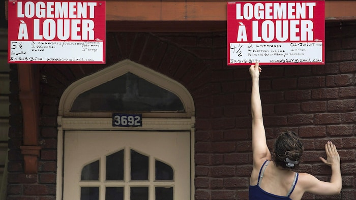 Une femme retire une pancarte « logement à louer » sur un immeuble.