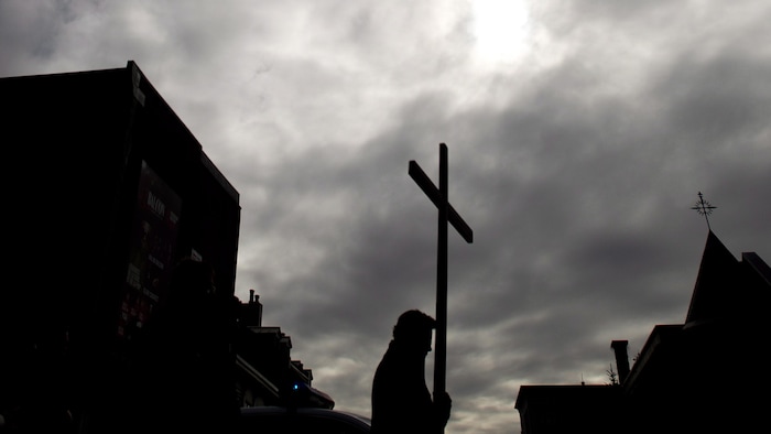 Un marcheur avec une croix sous un ciel gris.