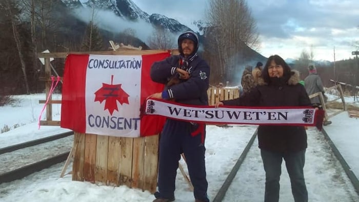 Dos manifestantes sostienen una pancarta en apoyo de los indígenas wet'suwet'en en el frío junto a la vía férrea cerca de New Hazelton, en Columbia Británica.
