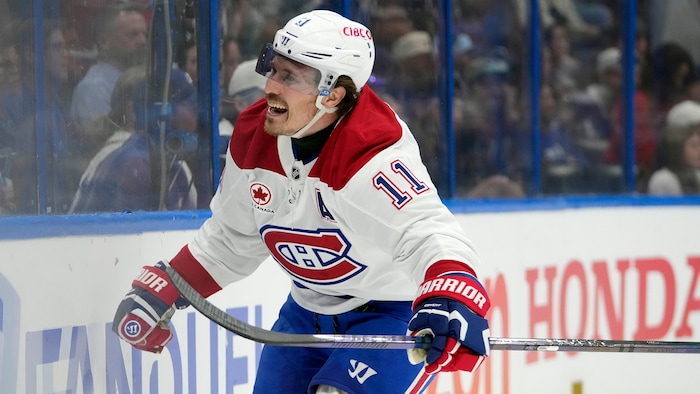 Vêtu de l'uniforme blanc du Canadien, il crie de joie en tenant son bâton dans sa main gauche.