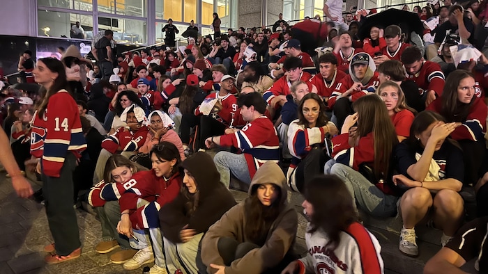 Des gens vêtus de chandails du Canadien de Montréal sont assis dans des marches d'escalier. 