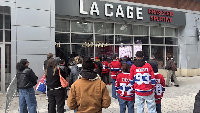 Des personnes à l'extérieur d'un bar regardent l'écran géant.
