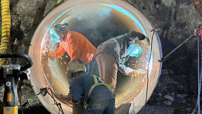 Trois hommes sont à l'intérieur d'une canalisation. Ils portent des masques et tiennent chacun un outil de soudure d'où jaillissent des étincelles.