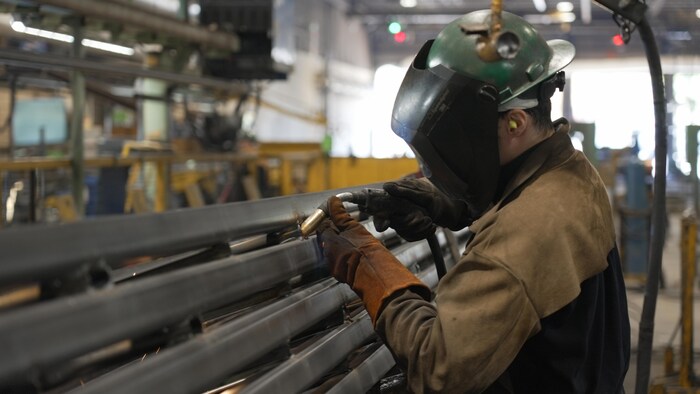 Un travailleur avec sa visière baissée travaille sur une poutrelle.