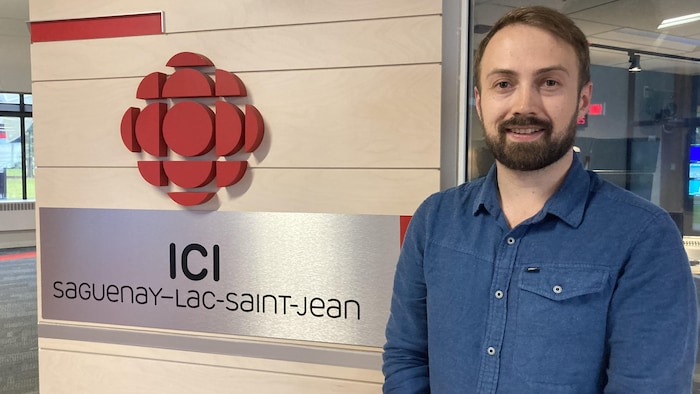 Un homme pose devant un mur avec un logo de Radio-Canada.