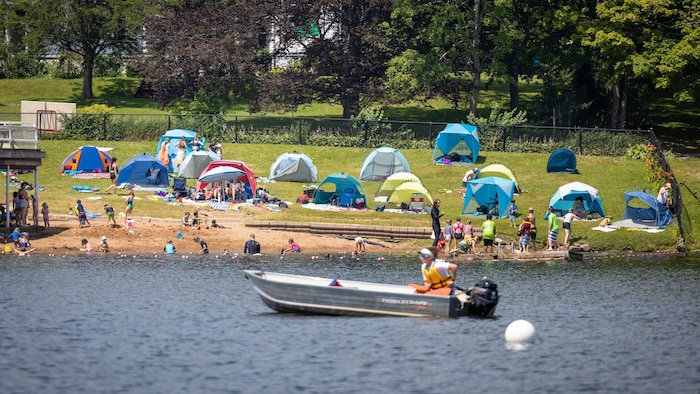 Des dizaines de personnes sur la plage et un petit bateau à moteur conduit par un sauveteur qui passe sur le lac.
