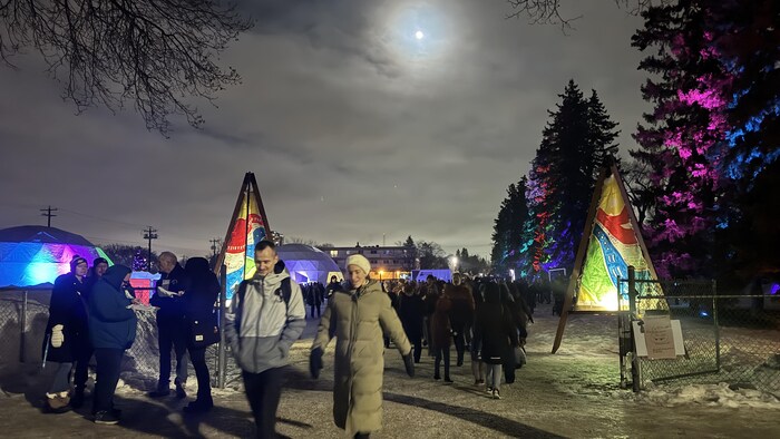 Des gens marchent sur un terrain enneigé où se trouve deux dômes avec des projections lumineuses.